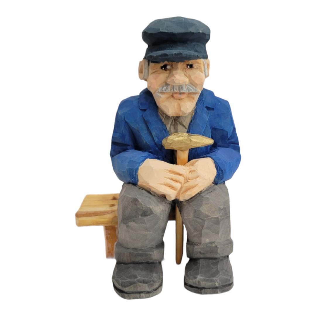 The "Elmer Axelson" figurine by Bill Erickson is a hand-painted, wood-carved representation of an older man. He is depicted in a blue jacket and cap, with a gentle smile, holding a cane while sitting comfortably on a wooden bench.