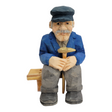The "Elmer Axelson" figurine by Bill Erickson is a hand-painted, wood-carved representation of an older man. He is depicted in a blue jacket and cap, with a gentle smile, holding a cane while sitting comfortably on a wooden bench.
