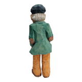 This 8 1/2 inch wood carved figure, titled "Man w/Pipe" by Bill Erickson, features a person with a green shirt, orange pants, black cap, and long white hair, viewed from the back.