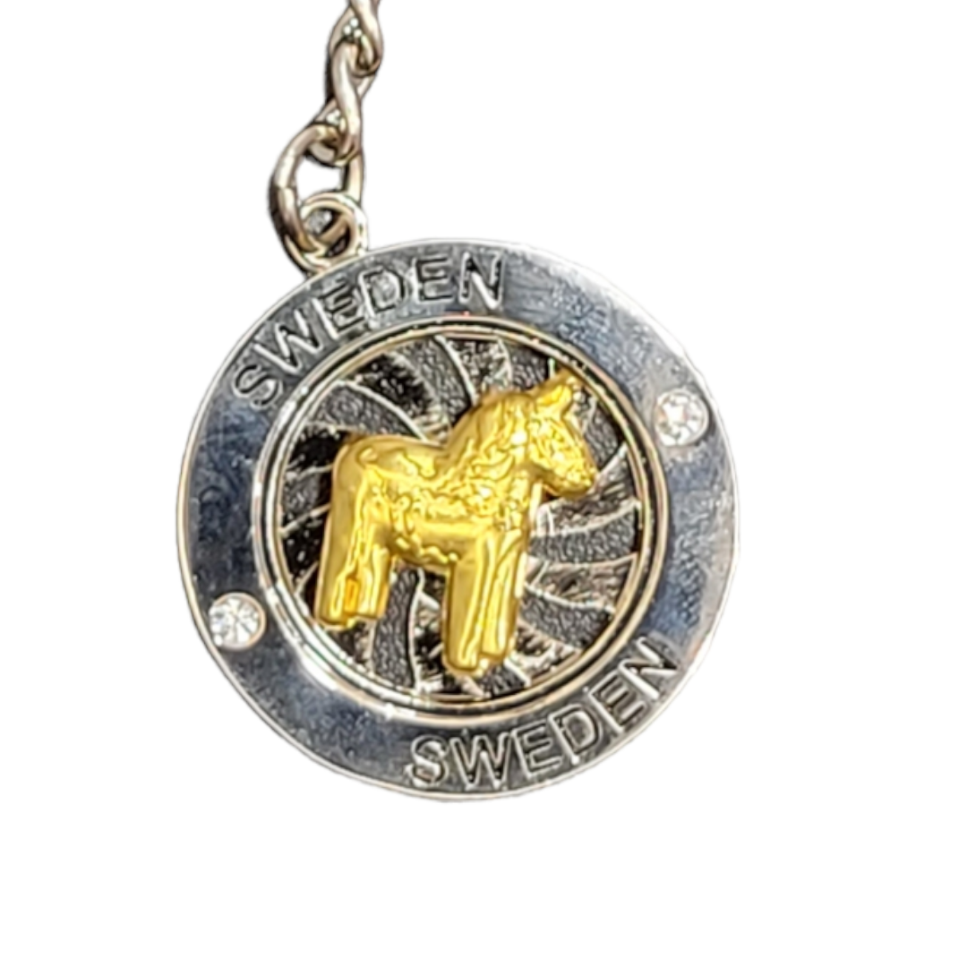 A circular metal keychain featuring a gold Dala Horse in the center, with Sweden engraved twice around the edge, named Spinner Key Chain with a Dala Horse in the Center.