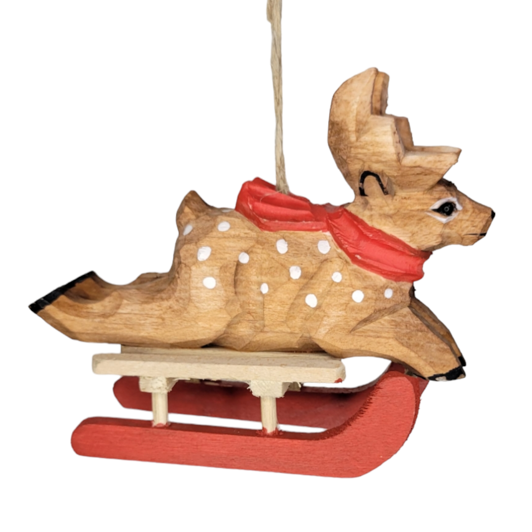 Introducing the Ornament: Wood Animals on Sled—a hand-painted wooden ornament featuring a delightful reindeer adorned with a red scarf, riding atop a vibrant red sled. The reindeer's body is charmingly decorated with white polka dots, making it an ideal addition to elevate your holiday décor in any setting.