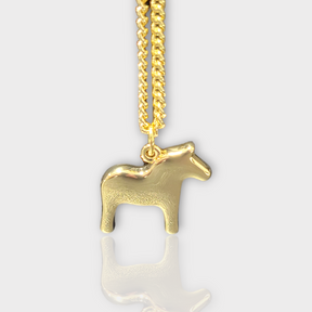 The Dala Horse Necklace by Anna Viktoria, featuring a gold horse-shaped pendant on a fine chain, embodies the elegance of Scandinavian jewelry and highlights the traditional Swedish symbol against a plain background.