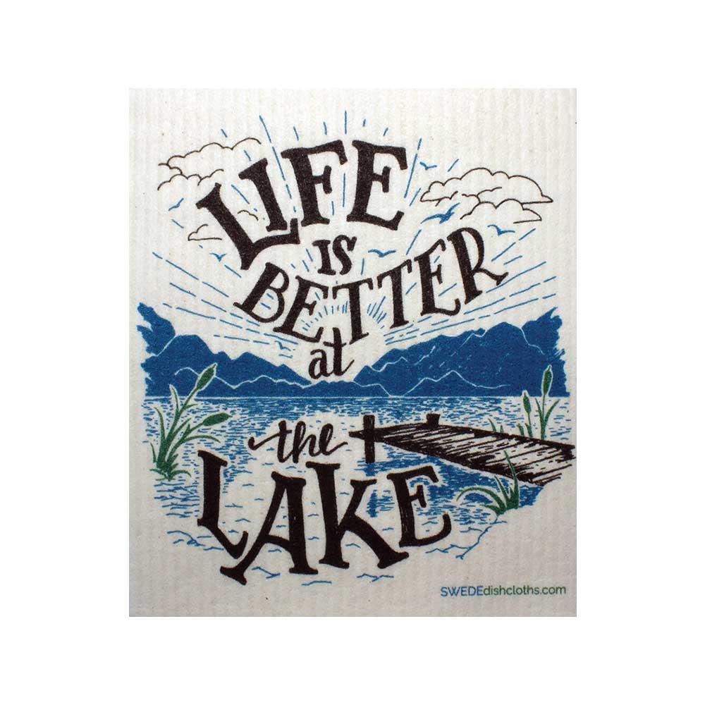 The "Life is Better at the Lake" Swedish Dish Cloth showcases text with an illustration of a wooden dock stretching into a serene lake, surrounded by clouds and lush plants. This design captures tranquility and sustainability, reflecting the eco-friendly nature of Swedish dishcloths crafted from sustainable raw materials.