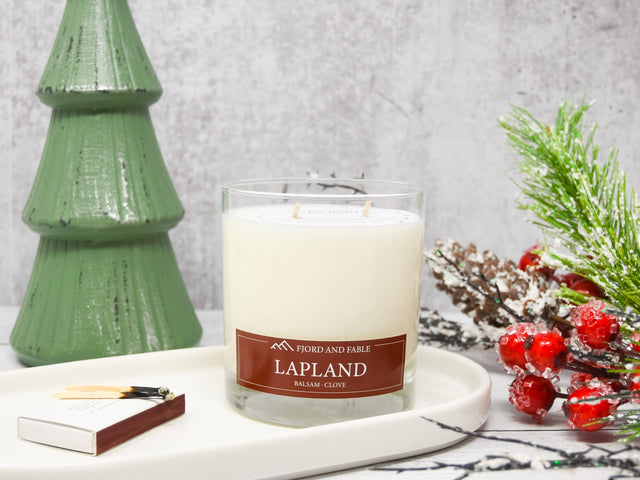 The Lapland Candle by Fjord & Fable features a balsam fir, clove, and cedar blend in an 8 oz glass with two wicks—perfect for creating a woodsy holiday atmosphere beside festive decor.