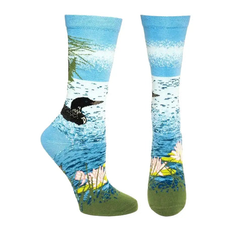 The Ozone Socks – Womens Loon Lake Crew Sock (One Size) features a scenic lake design with a black loon swimming among green reeds and pink water lilies on a blue and green background.