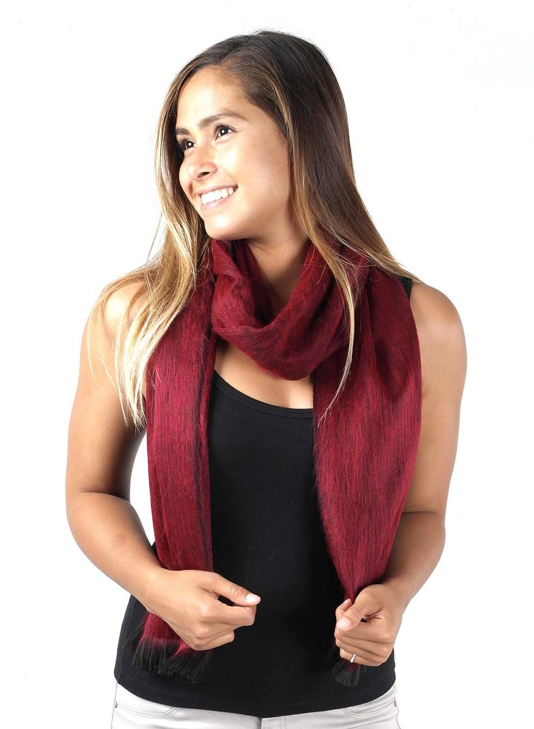 A woman in a black tank top and an Alpaca Scarf - Sapphire Red with Black Fringe stands against a white background, smiling as she looks to her left.