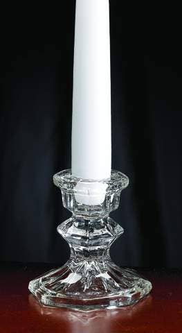 A single white taper candle is elegantly displayed in a clear, faceted Glass Taper Candle Holder on a dark background, which measures 3.75 inches in height and 7/8 inches in diameter.