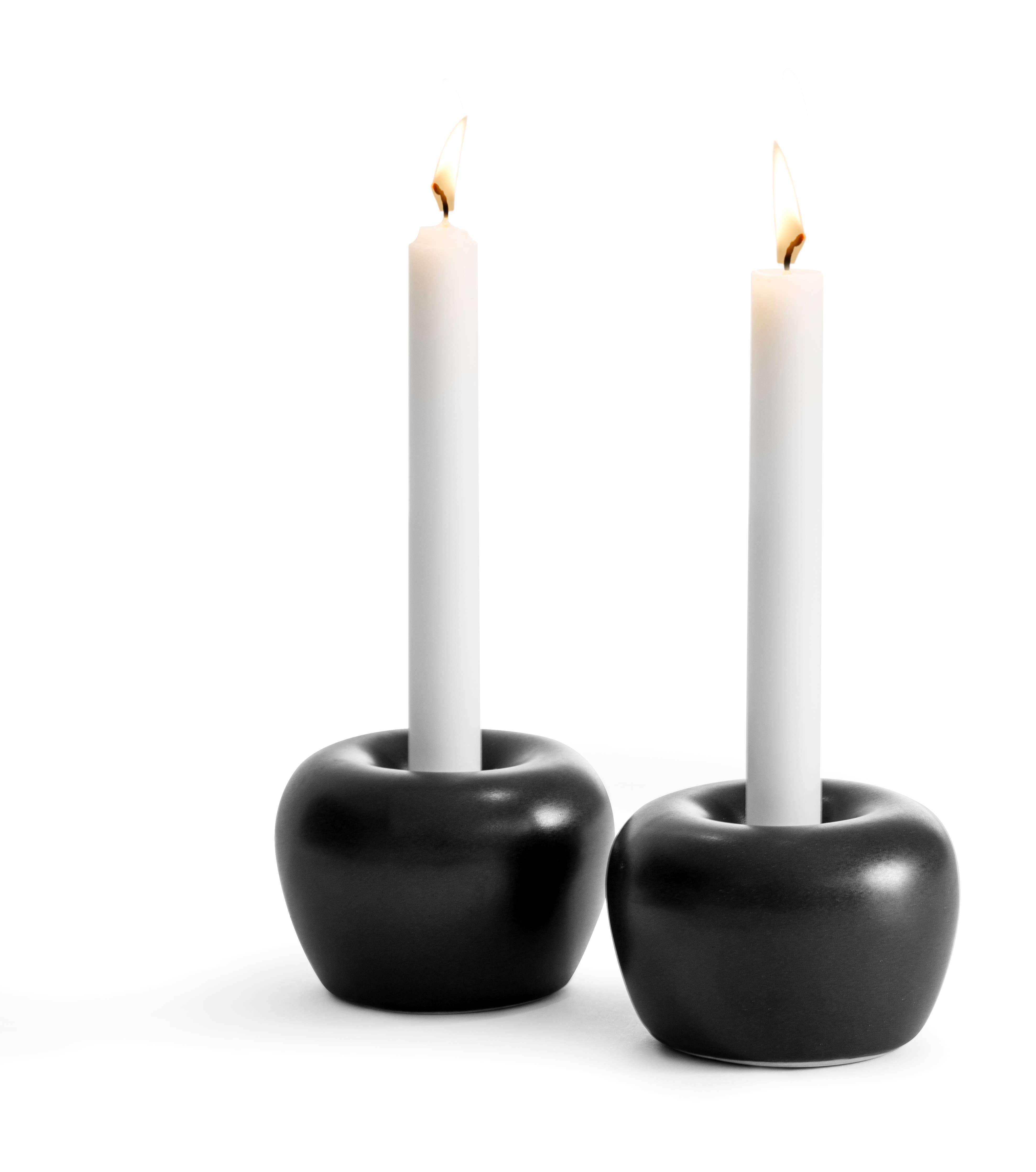 Two elegantly lit white candles sit in sleek black holders from the Apple Candleholder 2-Pack Mini Apple collection against a plain white background, reminiscent of Kim Vejsholts designs with a nod to timeless stoneware aesthetics.