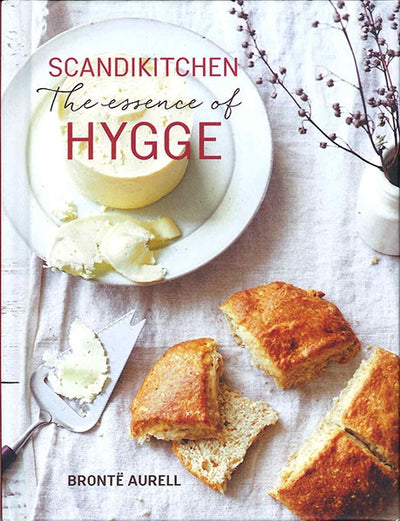 Cover of the book "ScandiKitchen: The Essence of Hygge" by Brontë Aurell, featuring Danish recipes along with bread and cheese on a plate, a knife, and sprigs.