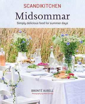 Cover of ScandiKitchen: Midsommar by Brontë Aurell features a summer dining table with flowers, dishes, and drinks set against a scenic field, embodying Scandinavian culinary traditions.