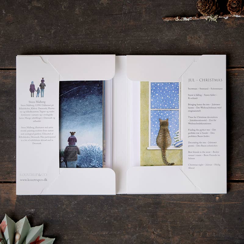 A set of cards featuring enchanting Scandinavian scenes, such as a person and a dog frolicking in the snow and a cat watching snowflakes from a window. The accompanying text elegantly conveys holiday themes, capturing the spirit found in the Christmas card collection by Steen Malberg Kostroupco, "Card Pack: Jul (Christmas) 8 cards, with envelopes.